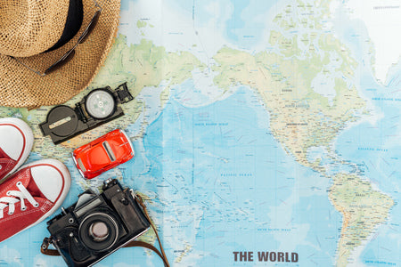 Main tenant une carte et un appareil photo argentique dans un décor de voyage